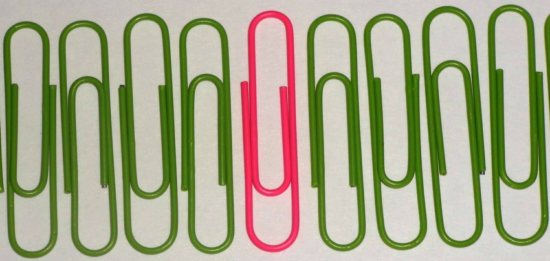 eight green paper clips with one pink in the middle